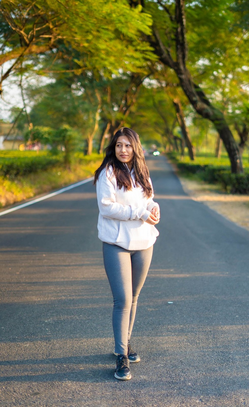 Loose white blouse, fitted grey jeans and dark trainers on a tree-lined road.