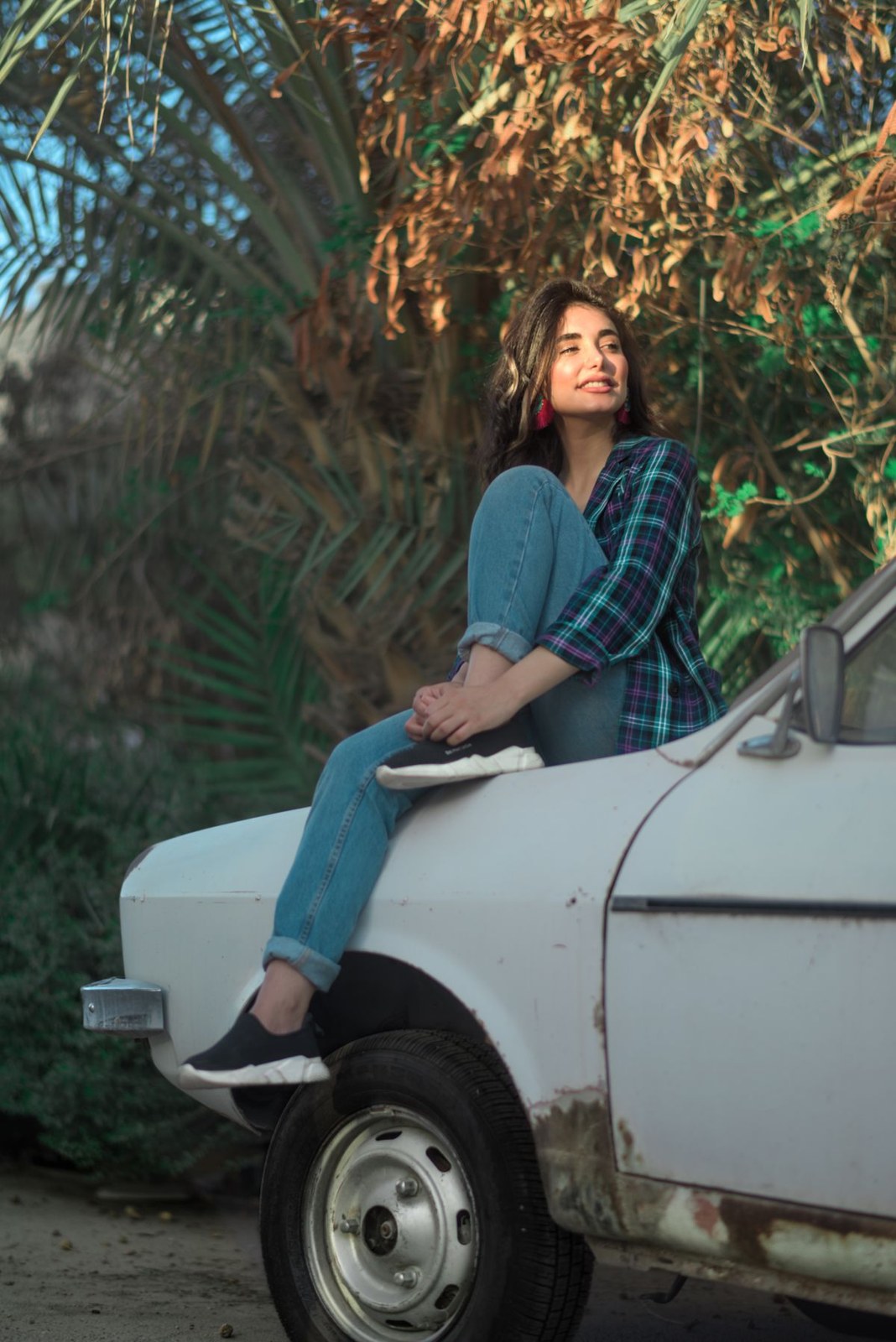 Dark blue-and-green checked shirt, blue jeans and black trainers, seated on a white vehicle.