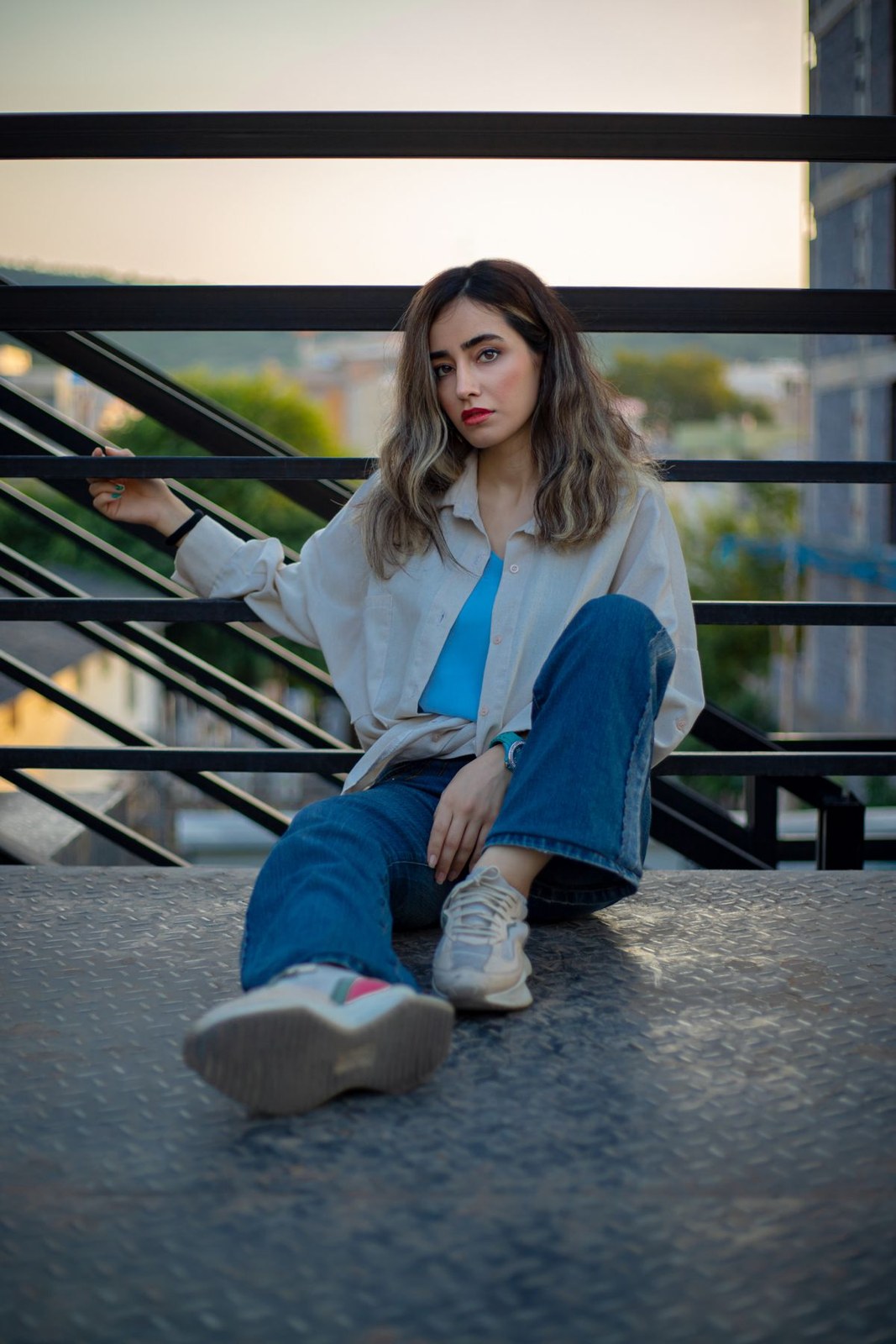 Pale open overshirt, bright-blue T-shirt, cuffed blue jeans and white trainers on steps.
