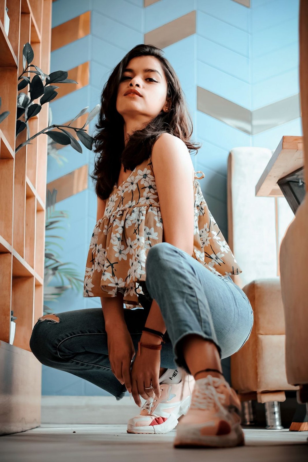 Loose floral sleeveless top, cuffed blue jeans and white patterned trainers.